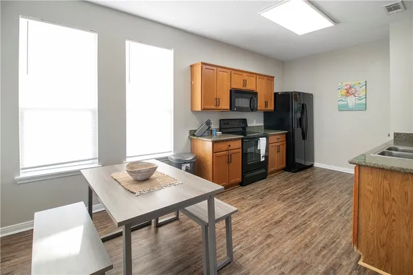 a kitchen with stainless steel appliances granite countertop a stove top oven a refrigerator a dining table and chairs with wooden floor