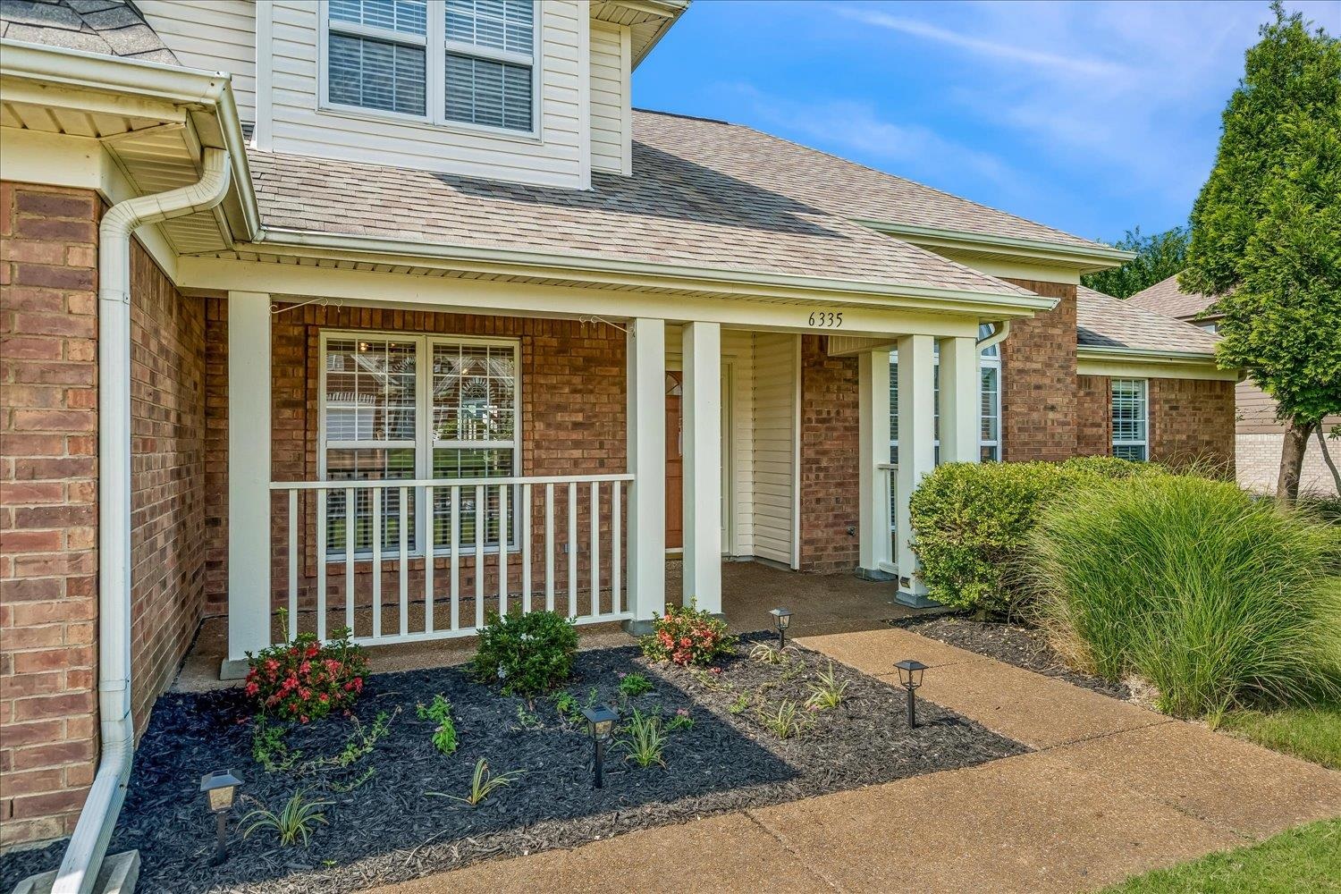 6335 Needle Ridge Road Bartlett, TN 38135 - Photo 2 of 25 Brick facade residence featuring a covered front porch with white railing, light-colored siding, and a gabled roof