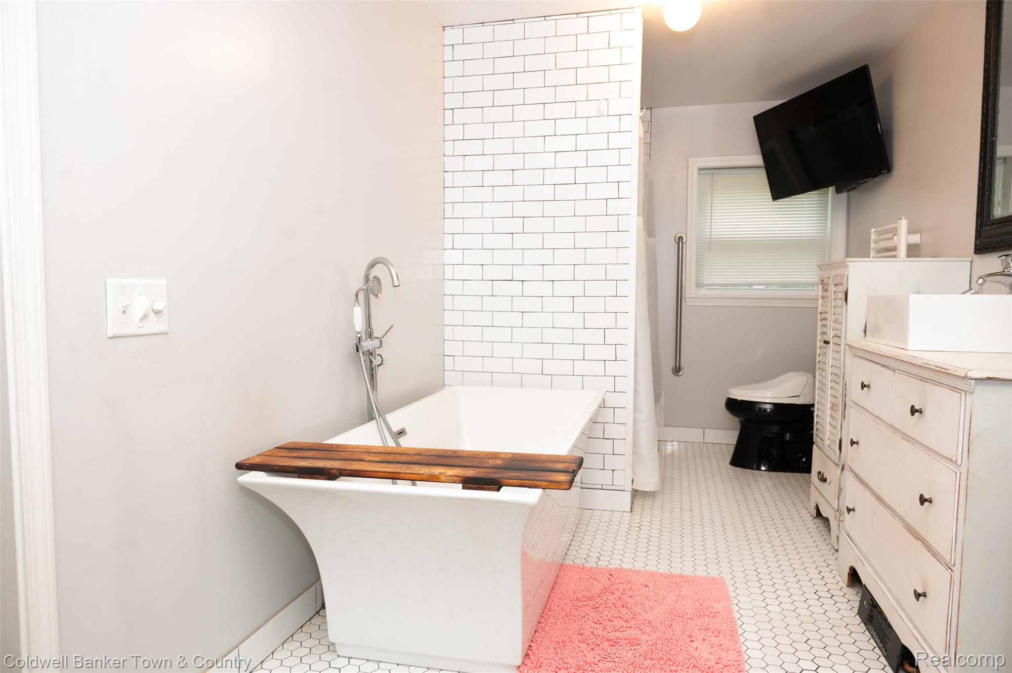 6150 North Fleming Road Howell, MI 48855 - Photo 21 of 23 Freestanding soaking tub with floor-mounted faucet, subway tile accent wall, white hexagonal floor tiling, and a vanity with an integrated sink