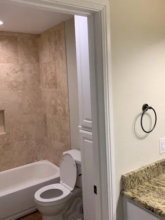 a bathroom with a granite countertop bathtub shower sink vanity and toilet