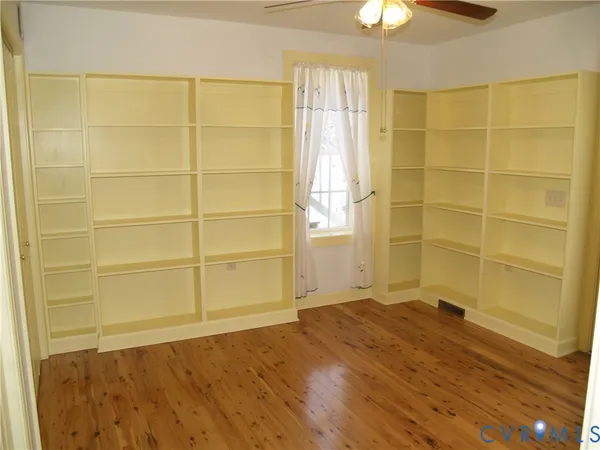 a view of empty room with wooden floor and fan