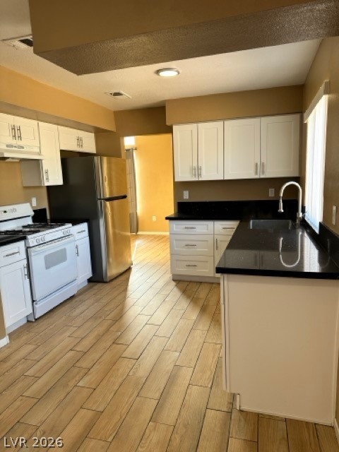4140 North Compass Rose Way Las Vegas, NV 89108 - Photo 5 of 16 Kitchen with white gas stove, white cabinets, wood tiled floors, dark stone counters, and freestanding refrigerator