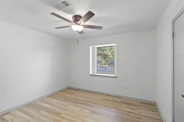 an empty room with wooden floor ceiling fan and windows