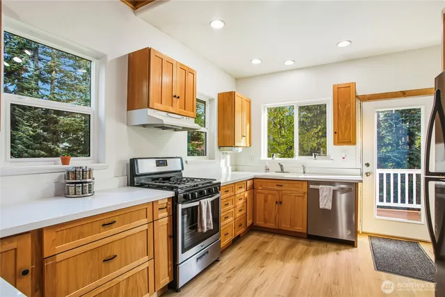 a kitchen with stainless steel appliances granite countertop wooden floor a sink a stove and a window