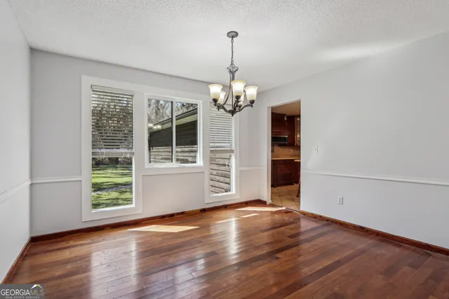 an empty room with wooden floor chandelier and windows