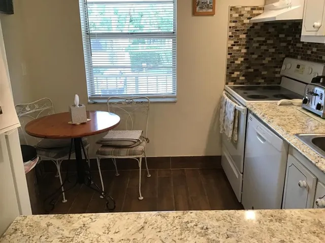 a kitchen with granite countertop a sink a stove a dining table and chairs