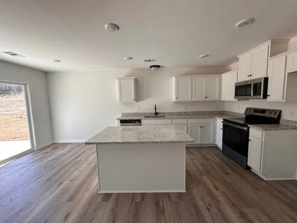 a kitchen with granite countertop a stove top oven a sink dishwasher and a microwave with wooden floor