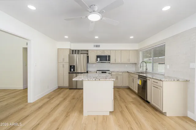a kitchen with stainless steel appliances granite countertop a refrigerator a stove top oven a sink dishwasher and white cabinets with wooden floor