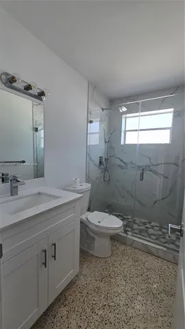 a bathroom with a granite countertop toilet a sink a mirror and a shower