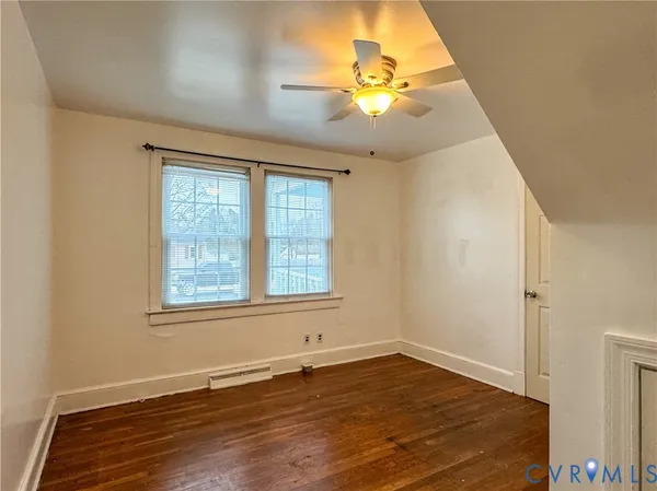 an empty room with wooden floor fan and windows