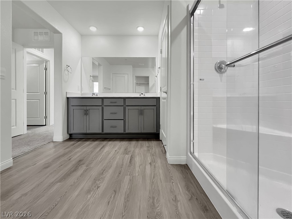 9984 Indigo Cliffs Street Las Vegas, NV 89141 - Photo 18 of 31 Bathroom featuring visible vents, a shower stall, double vanity, wood finished floors, and a sink