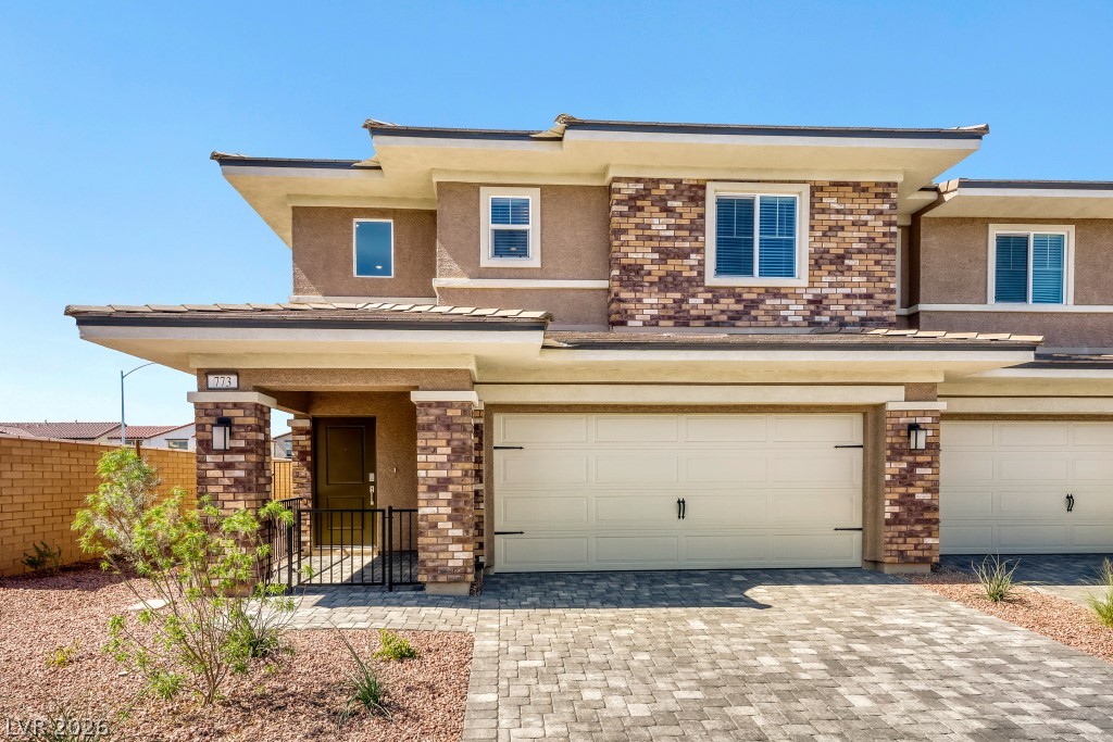 Prairie-style home with stucco siding, decorative driveway, and an attached garage