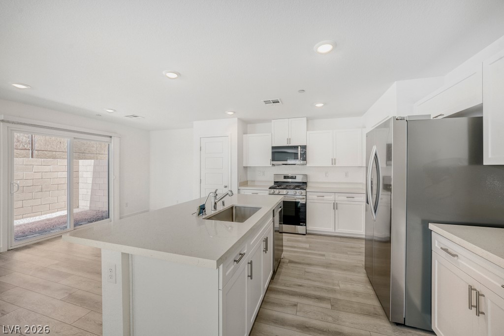 773 Fallen Phoenix Street Henderson, NV 89011 - Photo 10 of 28 Kitchen with stainless steel appliances, white cabinets, a kitchen island with sink, light wood-style floors, and recessed lighting