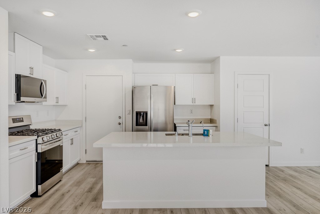 773 Fallen Phoenix Street Henderson, NV 89011 - Photo 12 of 28 Kitchen with stainless steel appliances, a kitchen island with sink, white cabinets, light wood-style flooring, and recessed lighting