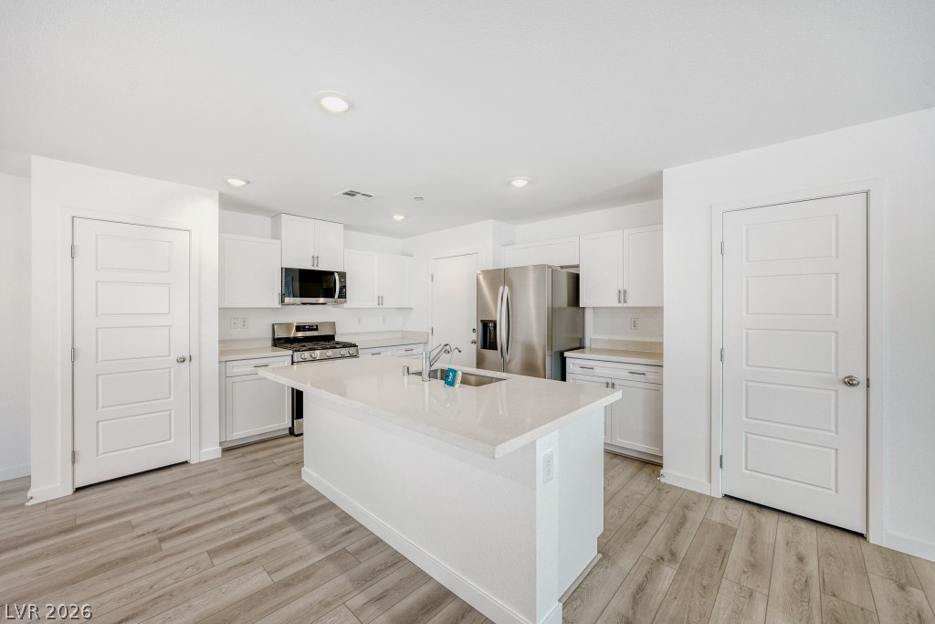 773 Fallen Phoenix Street Henderson, NV 89011 - Photo 9 of 28 Kitchen featuring stainless steel appliances, white cabinetry, light wood finished floors, a center island with sink, and recessed lighting