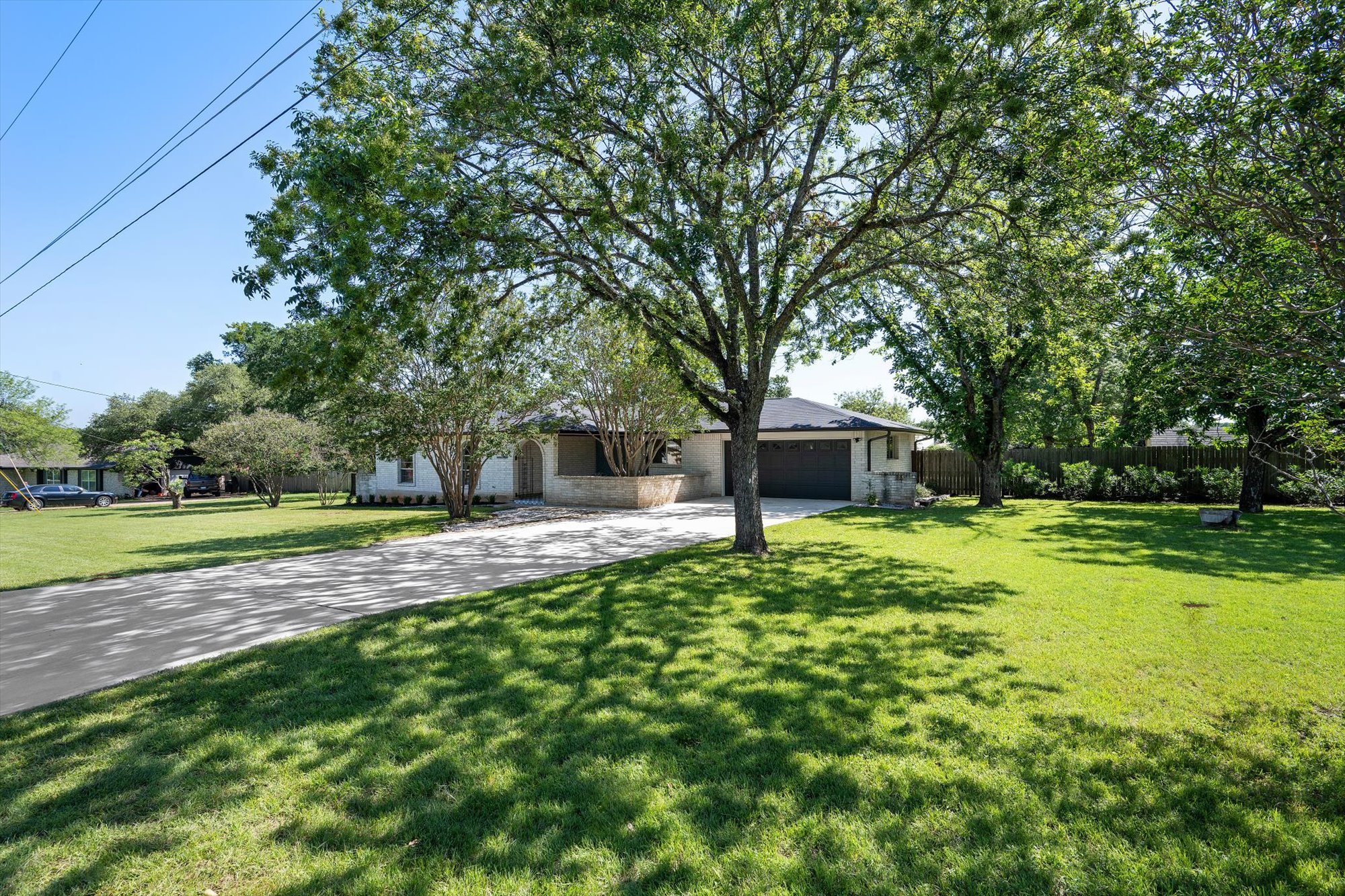109 Woodland Road Georgetown, TX 78628 - Photo 13 of 40 Mature trees shade a charming brick and stone residence, featuring a welcoming driveway and well-kept lawn.