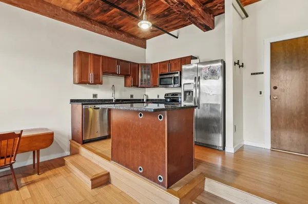 a kitchen with stainless steel appliances granite countertop a stove a refrigerator a sink a dining table and chairs with wooden floor