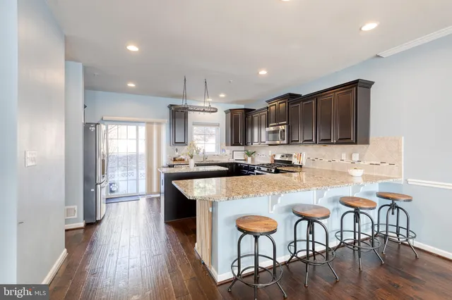 a kitchen with stainless steel appliances granite countertop a stove top oven a sink dishwasher a dining table and chairs with wooden floor