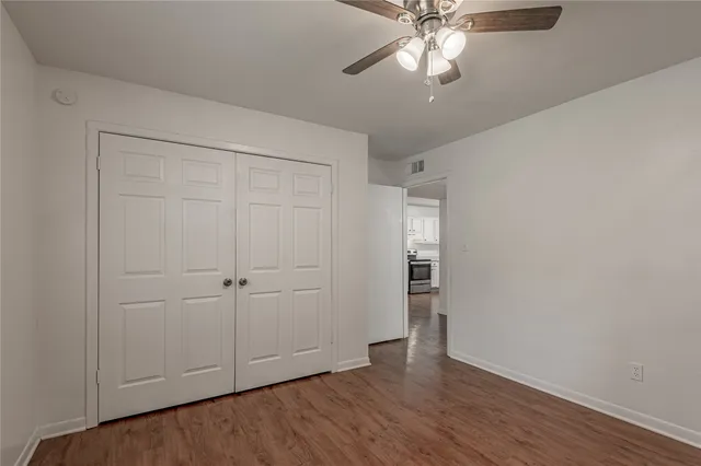 a view of an empty room with wooden floor and a ceiling fan