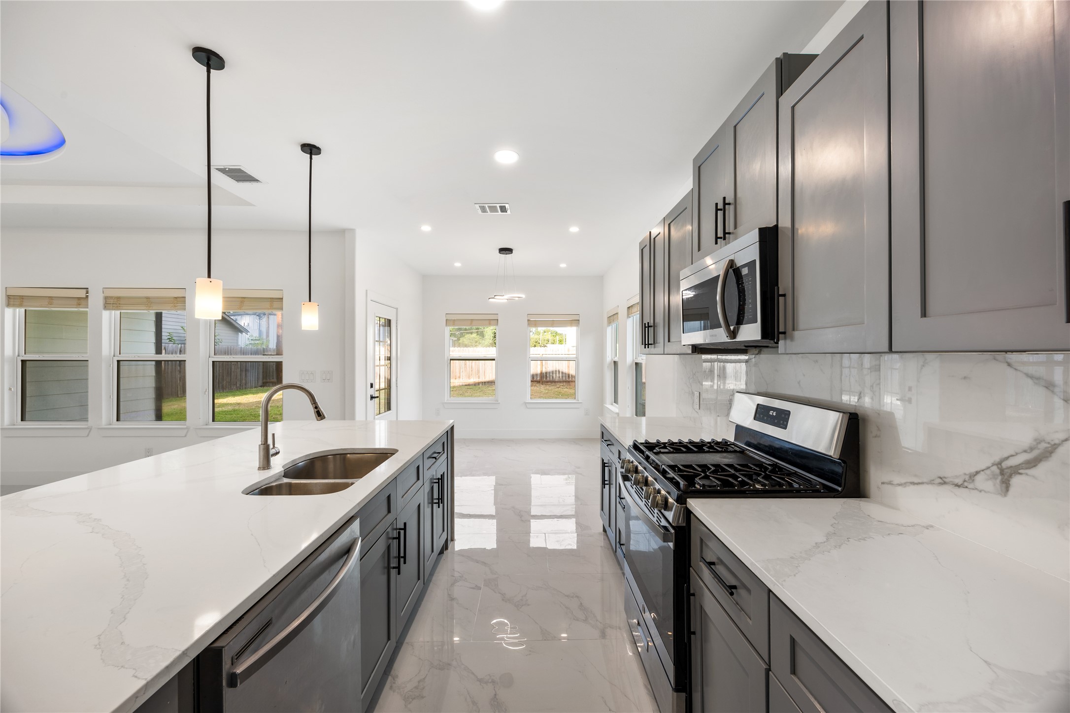 1121 Austin Street Rosenberg, TX 77471 - Photo 21 of 44 This modern kitchen features sleek gray cabinetry, stainless steel appliances, and a spacious quartz countertop island with a built-in sink. Bright and airy with ample natural light from large windows, it offers an open layout ideal for cooking and entertaining.