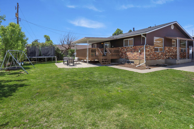 5108 South 2000th Street West Roy, UT 84067 - Photo 52 of 61 Rear view of house with a deck, a trampoline, a lawn, and brick siding