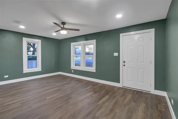 an empty room with wooden floor ceiling fan and windows