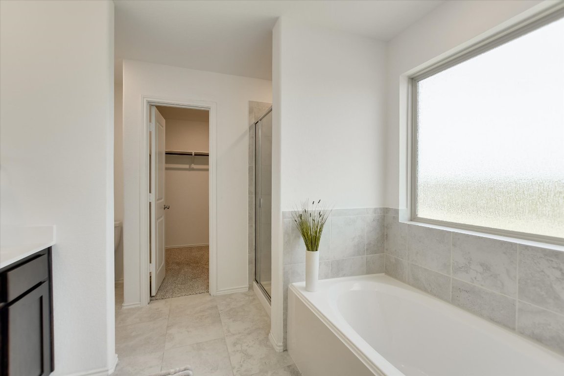 561 Greatest Gift Way Jarrell, TX 76537 - Photo 16 of 32 Bathroom featuring a stall shower, a bath, vanity, a spacious closet, and baseboards
