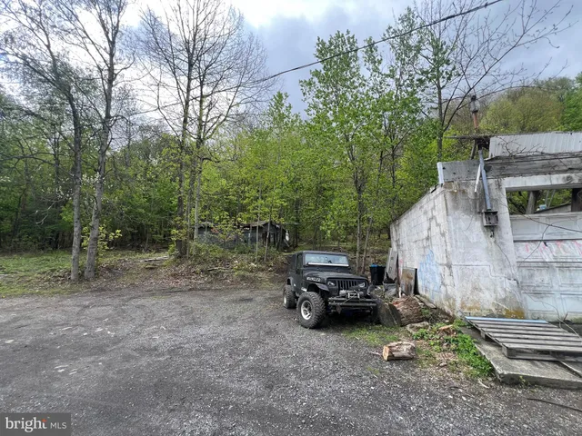 a view of a house with truck parked on a road near a forest