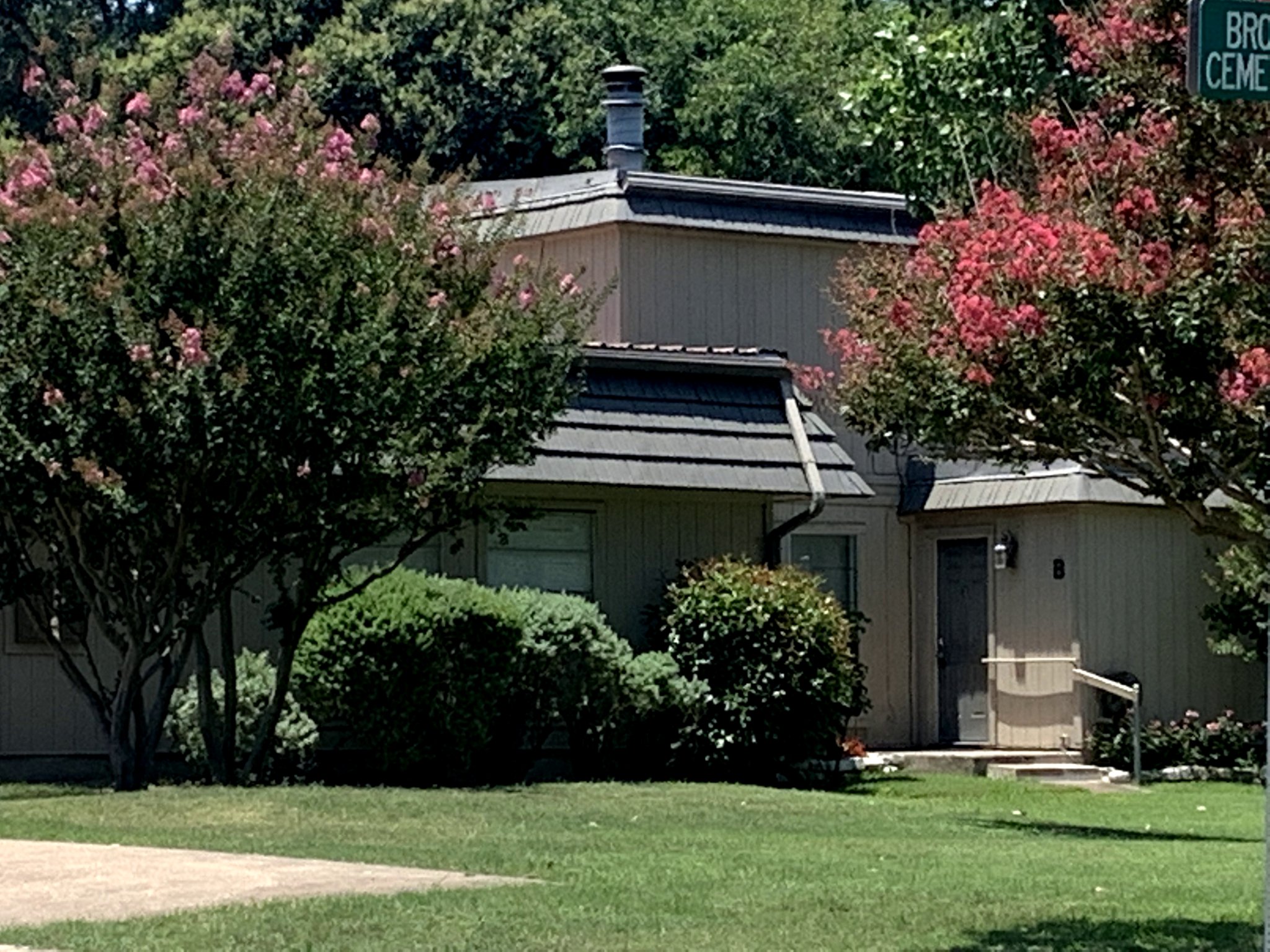 A modest residence nestled amidst flowering trees and well-maintained shrubbery.