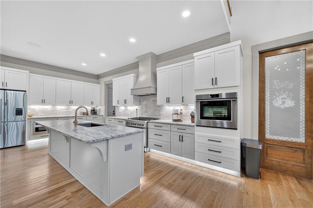 4726 Crestview Way Flowery Branch, GA 30542 - Photo 13 of 48 a kitchen with stainless steel appliances kitchen island granite countertop a stove top oven a sink dishwasher a refrigerator and white cabinets with wooden floor