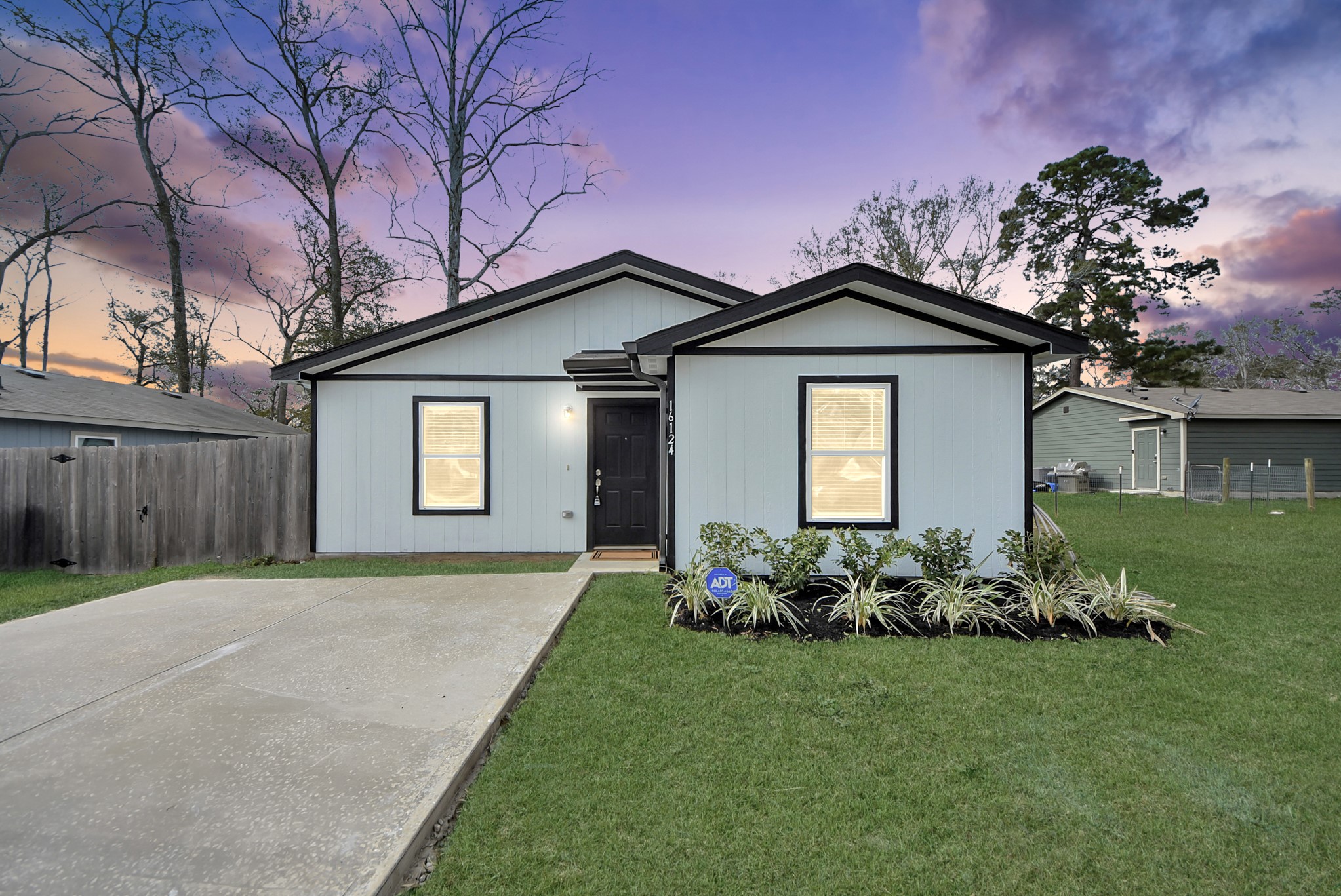 Charming single-story home with a modern exterior, featuring a fresh white facade with contrasting black trim. It has a neat front yard with simple landscaping and a newly added spacious driveway.