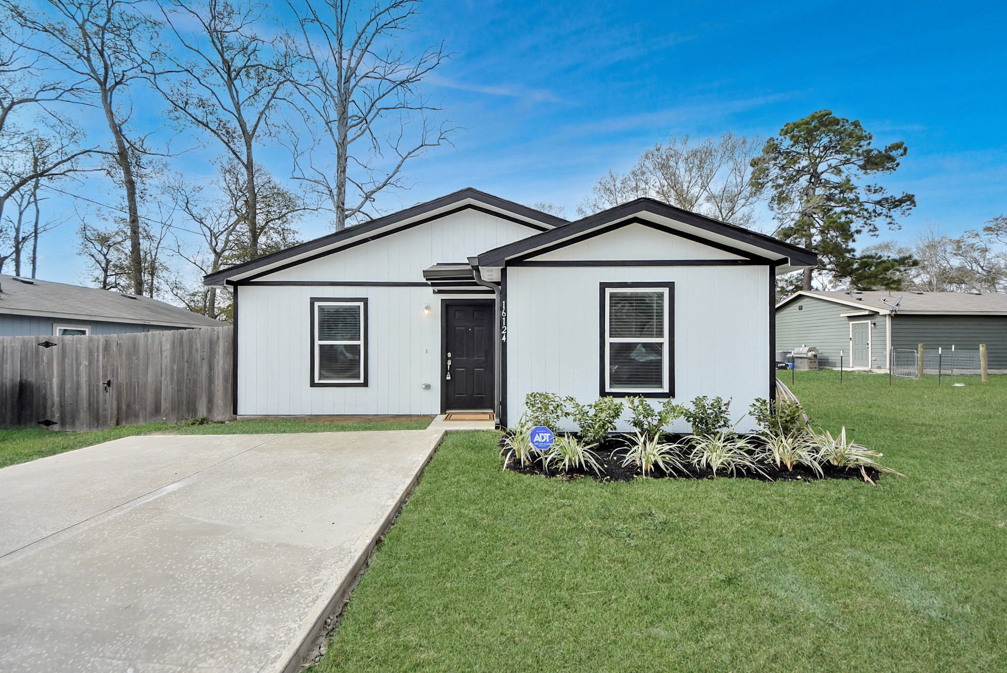 16124 Brettwood Lane Splendora, TX 77372 - Photo 2 of 40 Charming single-story home with a modern exterior, featuring a fresh white facade with contrasting black trim. It has a neat front yard with simple landscaping and a newly added spacious driveway.