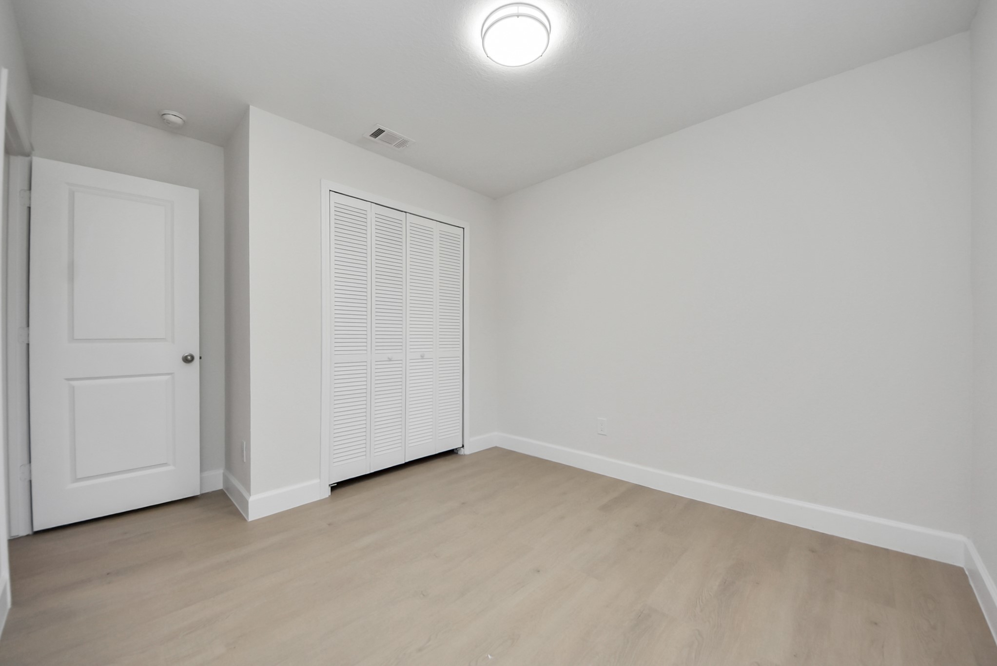 16124 Brettwood Lane Splendora, TX 77372 - Photo 23 of 40 This photo shows a clean, unfurnished room with light-colored wood flooring, neutral walls, a ceiling light, and a closed closet with louvered doors. It's simple and bright, offering a blank canvas for personalization.