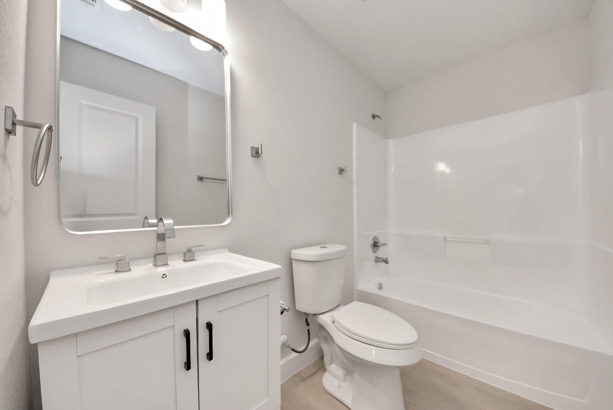 16124 Brettwood Lane Splendora, TX 77372 - Photo 25 of 40 This bathroom features a modern design with a clean, white aesthetic. It includes a sleek vanity with a large mirror, a toilet, and a bathtub with a shower. The space is bright and minimalist, ideal for a contemporary home.