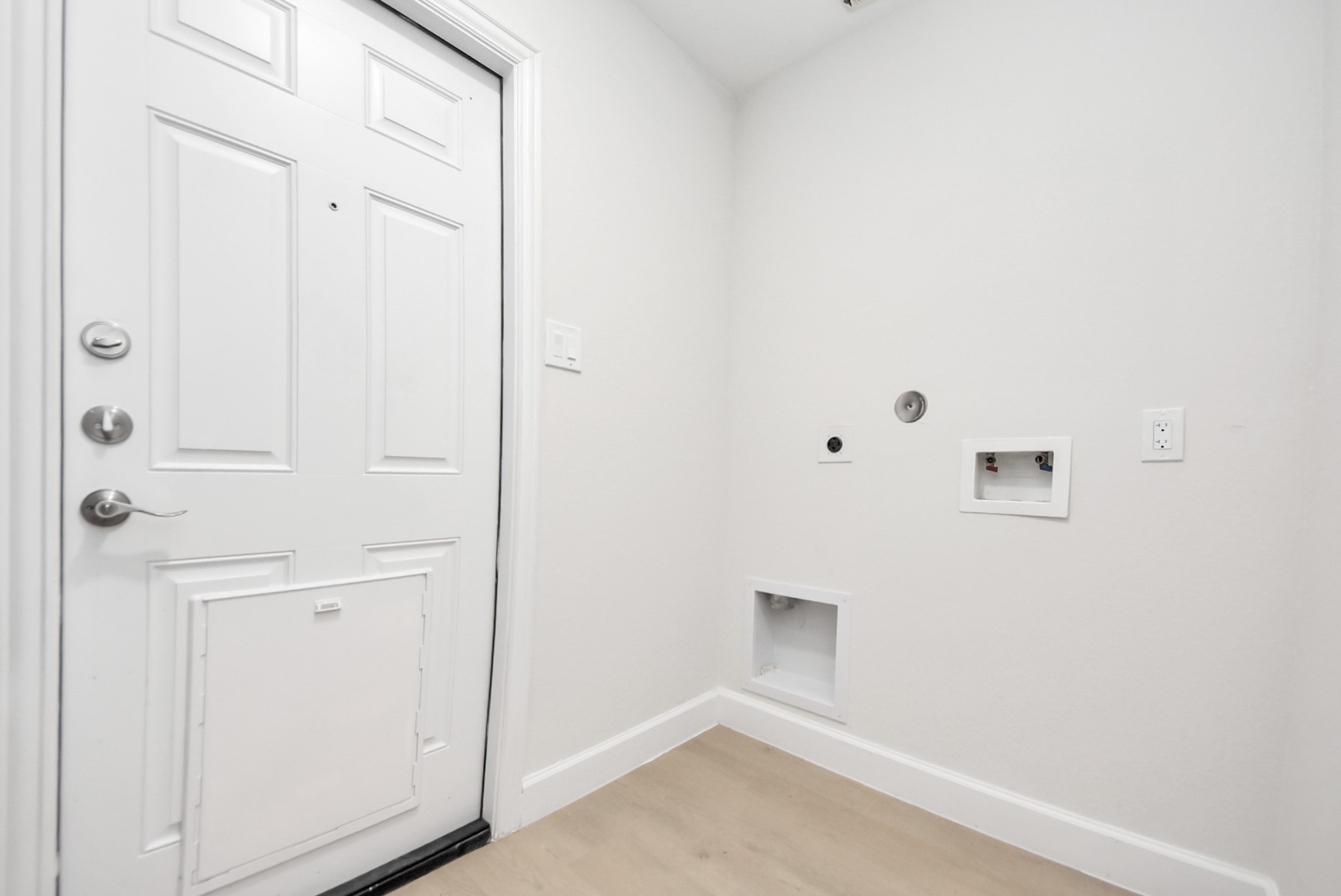 16124 Brettwood Lane Splendora, TX 77372 - Photo 27 of 40 This photo shows a laundry area with hookups for a washer and dryer. It features a white entry door with a pet door, neutral walls, and light wood flooring, providing a clean and functional space.