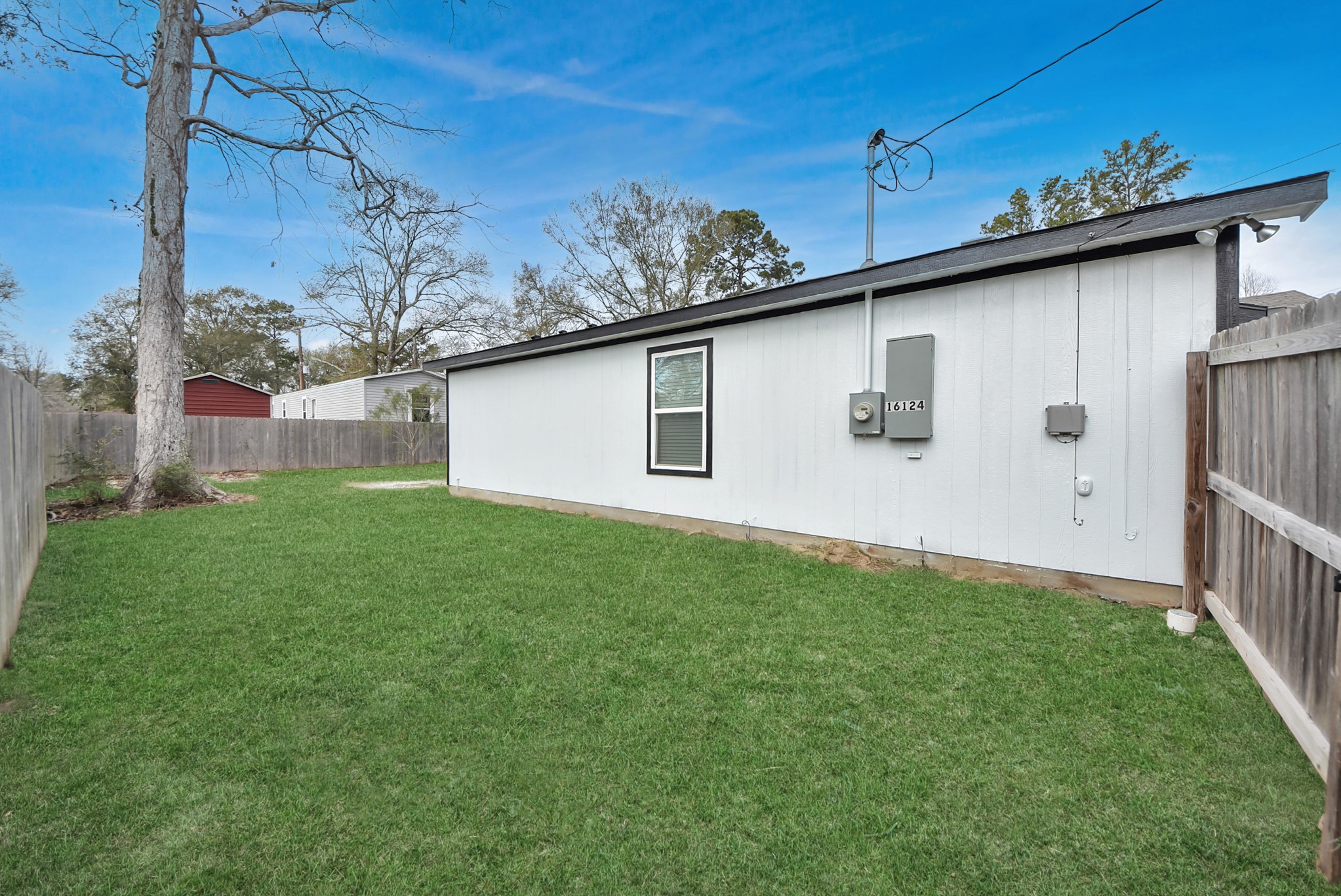 16124 Brettwood Lane Splendora, TX 77372 - Photo 30 of 40 Spacious backyard with a well-maintained lawn, surrounded by a wooden fence for privacy. The house has a modern exterior with a single window and utility connections visible. Perfect for outdoor activities or gardening.