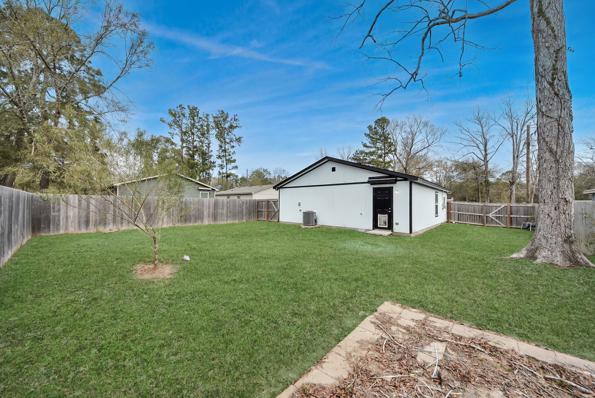 16124 Brettwood Lane Splendora, TX 77372 - Photo 32 of 40 Spacious backyard with a well-maintained lawn, mature trees, and a privacy fence. The house features a modern exterior and a separate storage or utility building. Ideal for outdoor activities and relaxation.