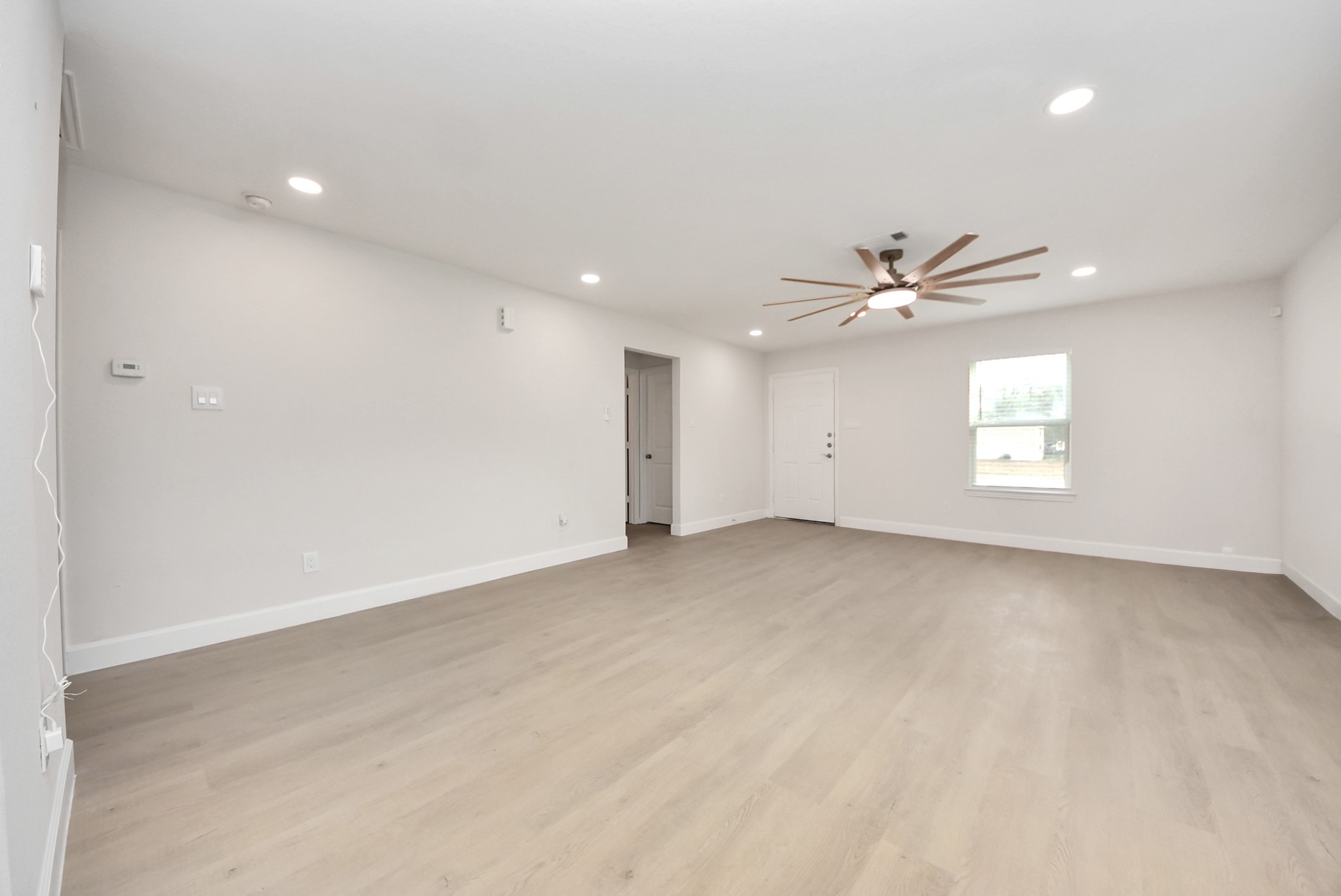 16124 Brettwood Lane Splendora, TX 77372 - Photo 6 of 40 This spacious living room features light wood flooring, neutral walls, recessed lighting, and a modern ceiling fan. It's bright and airy with a window and door providing natural light.