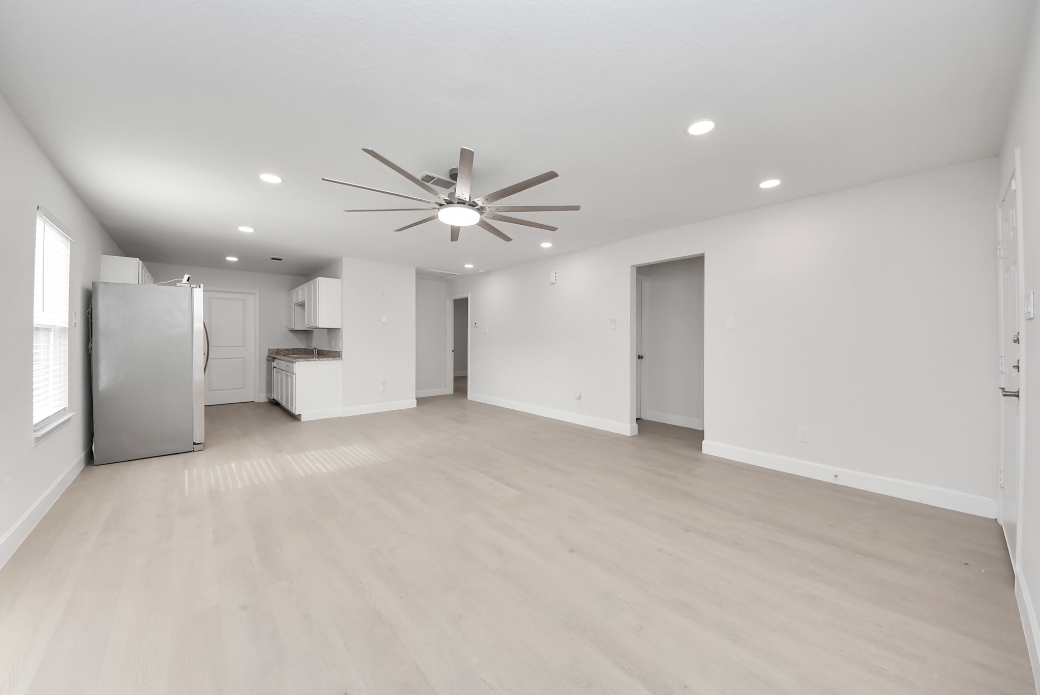 16124 Brettwood Lane Splendora, TX 77372 - Photo 7 of 40 This photo showcases a bright, open-concept living area with light wood flooring and recessed lighting. It includes a modern ceiling fan and a kitchen with white cabinetry and stainless steel appliances, creating a contemporary and inviting space.