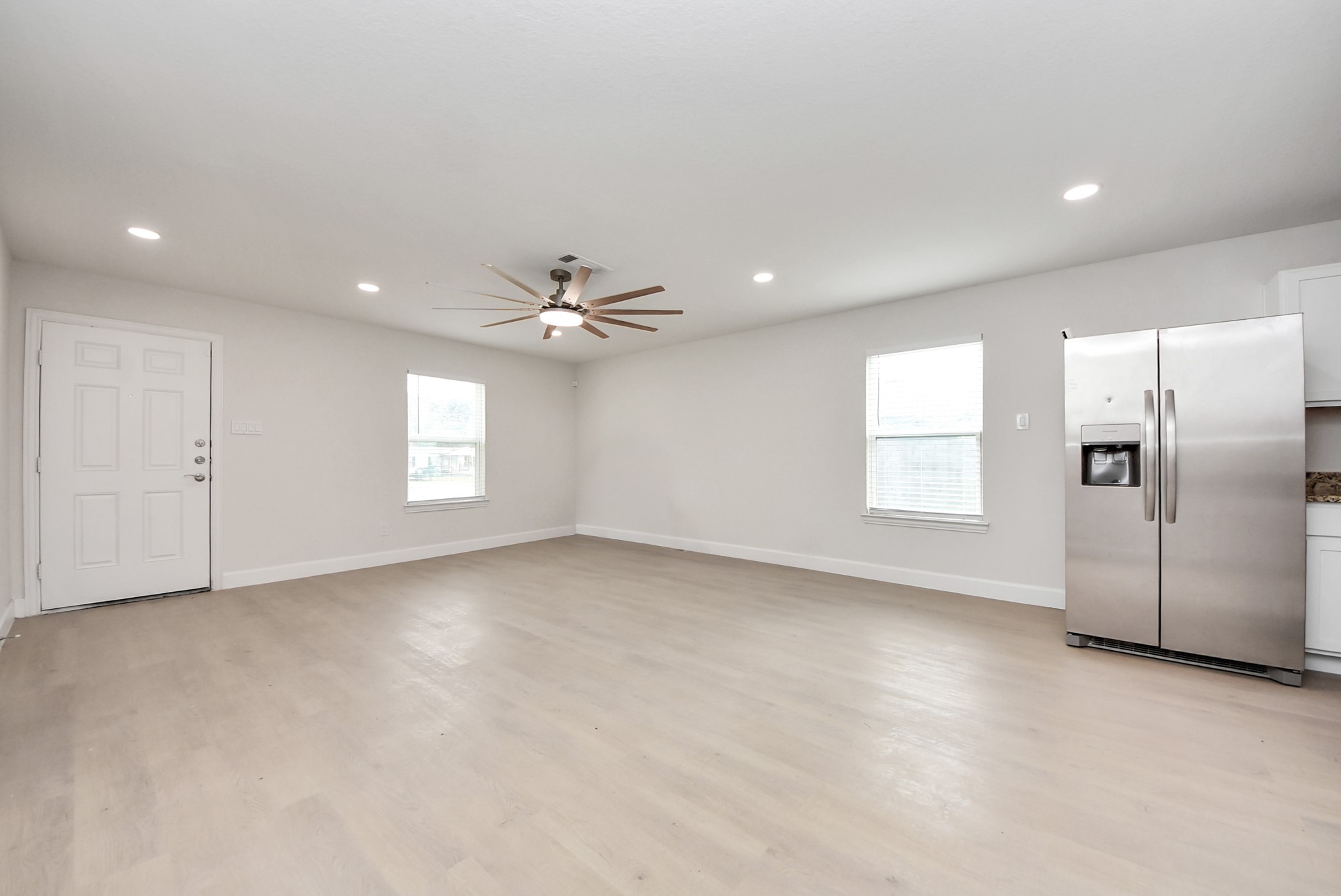 16124 Brettwood Lane Splendora, TX 77372 - Photo 8 of 40 This spacious, bright room features light wood flooring and recessed lighting. It includes a modern ceiling fan, two windows for natural light, and a stainless steel refrigerator, giving it a contemporary feel.