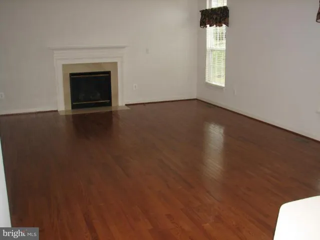 an empty room with wooden floor fireplace and windows