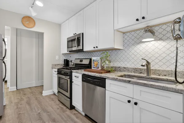 a kitchen with stainless steel appliances granite countertop white cabinets a sink a stove a refrigerator and microwave with wooden floor