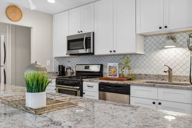 a kitchen with stainless steel appliances granite countertop a stove a sink and a white cabinets