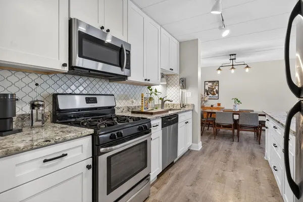 a kitchen with stainless steel appliances granite countertop a stove top oven a sink dishwasher a dining table and chairs with wooden floor