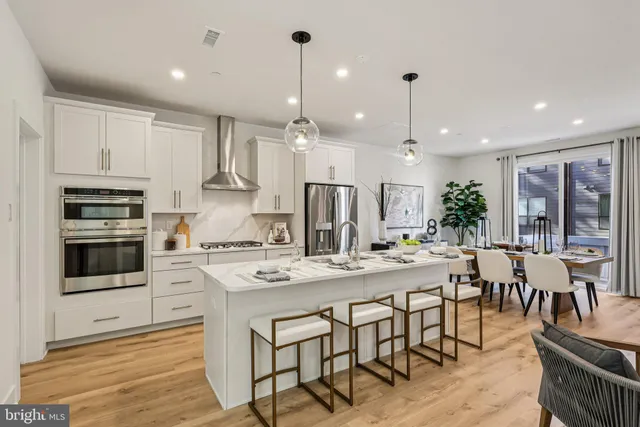 a kitchen with stainless steel appliances kitchen island granite countertop a refrigerator a sink dishwasher a dining table and chairs with wooden floor