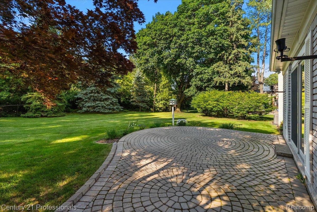 633 Foxhall Road Bloomfield Hills, MI 48304 - Photo 11 of 61 Expansive backyard featuring a circular paver patio, a manicured lawn, mature trees, and a house exterior with vertical siding and multiple windows