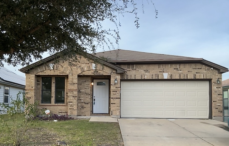 View of front facade featuring brick siding, driveway, an attached garage, and a shingled roof