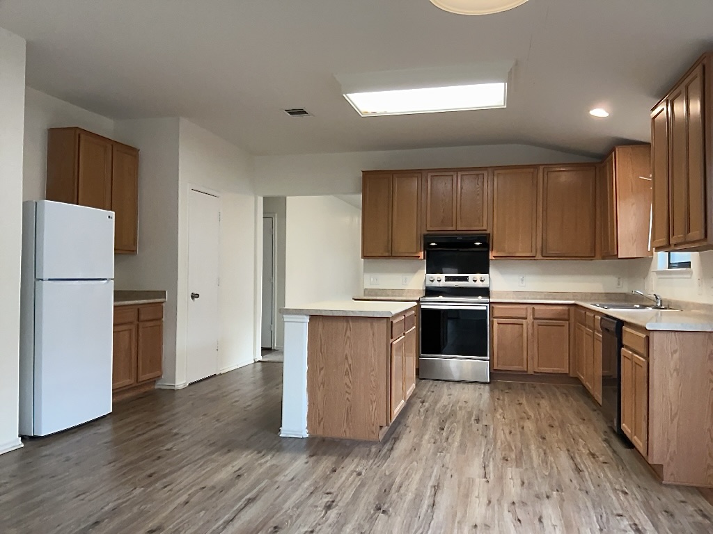 704 Big Sur Trail Taylor, TX 76574 - Photo 7 of 18 Kitchen with light countertops, electric range, freestanding refrigerator, light wood-type flooring, and lofted ceiling