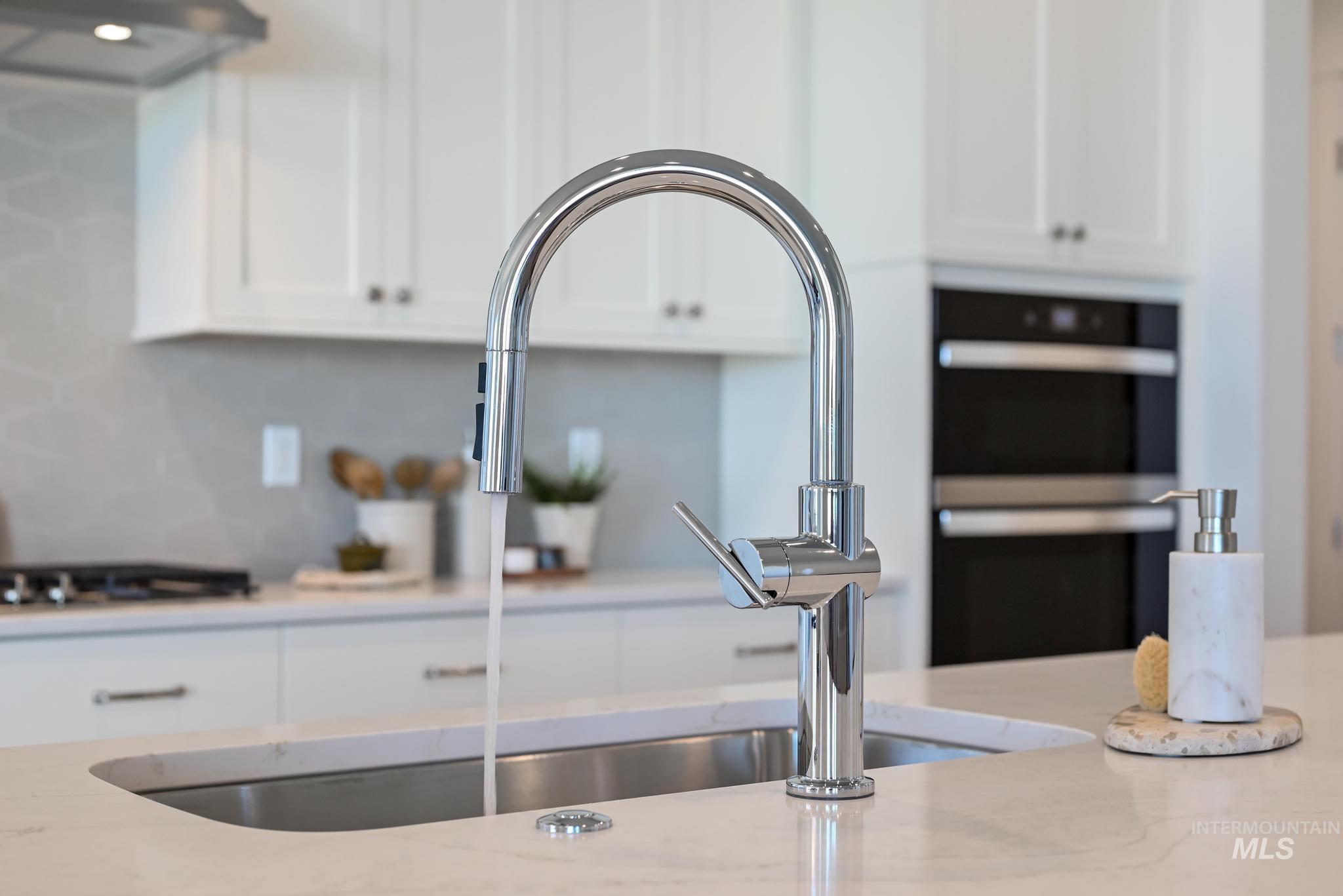 14676 Serenity Pt Street Caldwell, ID 83607 - Photo 13 of 41 Kitchen island featuring a single-basin stainless steel sink, polished chrome gooseneck faucet, light-toned countertop, and white shaker-style cabinetry with dark hardware
