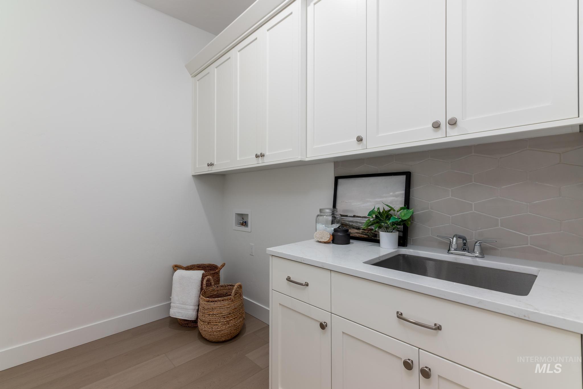 14676 Serenity Pt Street Caldwell, ID 83607 - Photo 27 of 41 Laundry area featuring extensive white shaker cabinetry, an integrated stainless steel sink, a light-toned countertop, and a gray geometric tile backsplash
